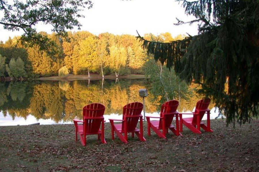 Red adirondack chairs on a lake in the fall